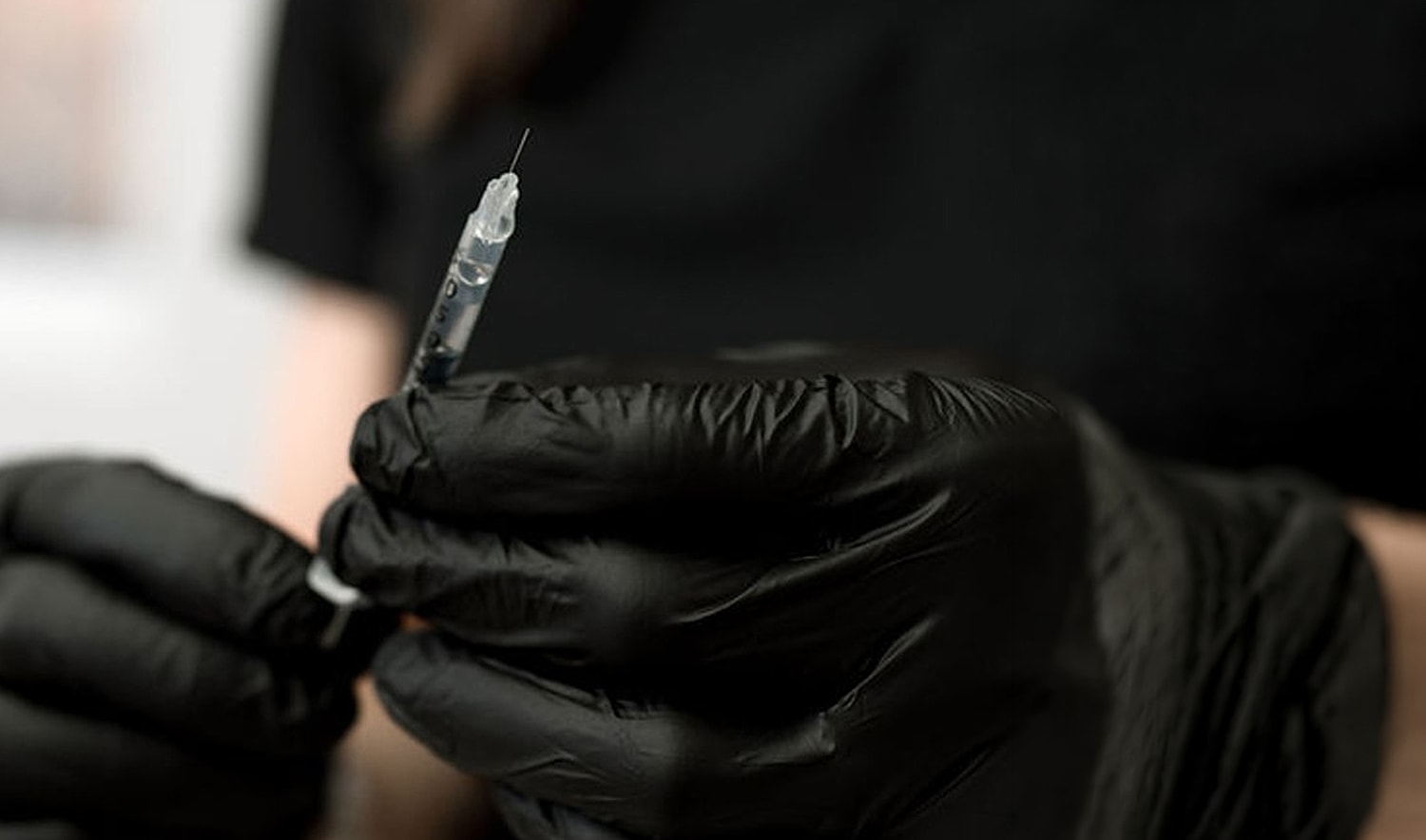 Gloved hands holding a syringe ready for injection.